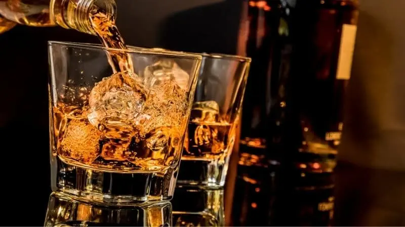 Rượu Whisky đang được rót ra trong cốc chứa đá lạnh