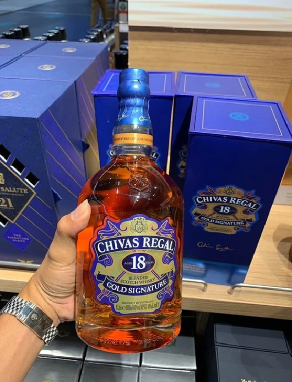 Trên tay cầm rượu Chivas Regal 18, bên sau là hộp đựng